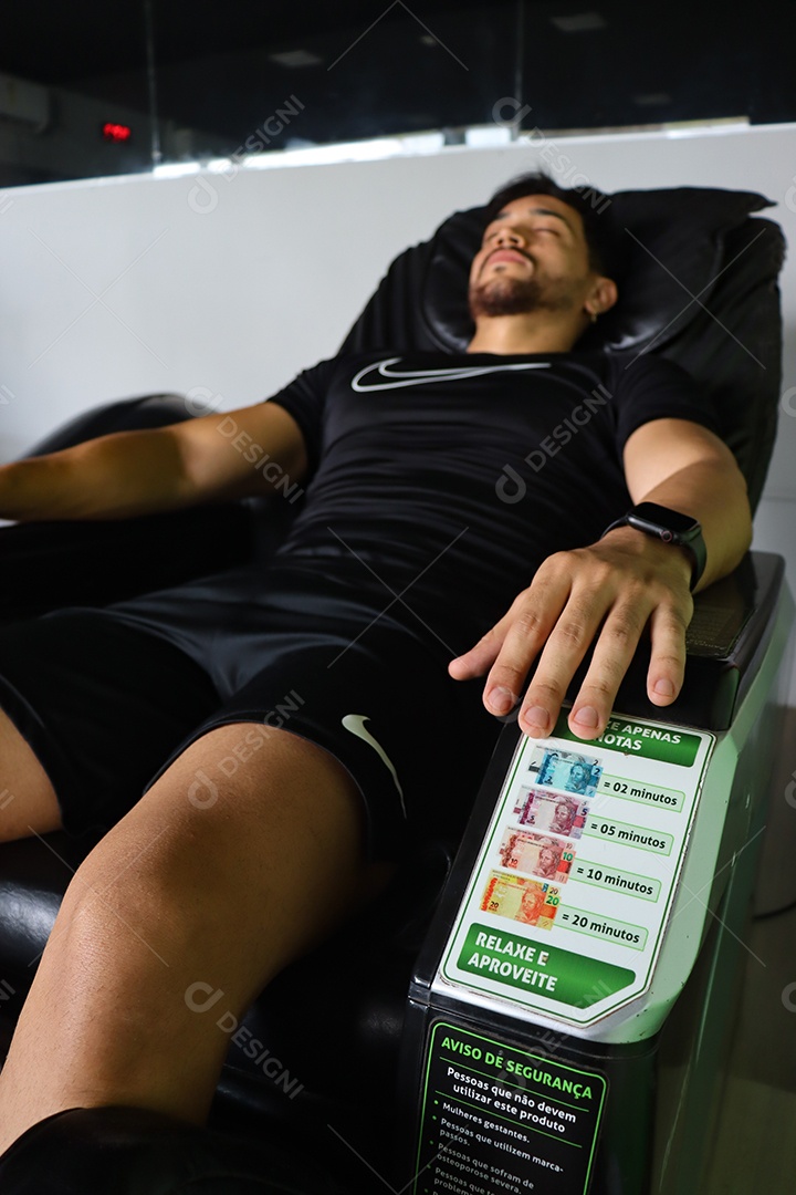 Belo homem deitado em poltrona de massagem sobre uma academia