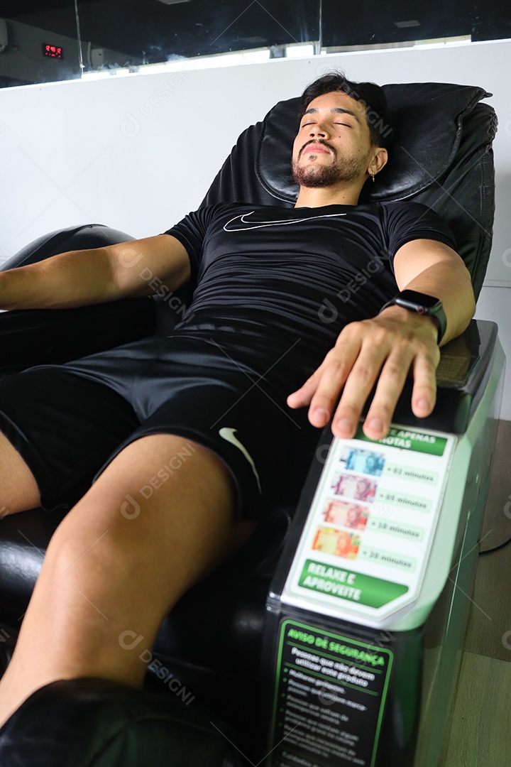 Belo homem deitado em poltrona de massagem sobre uma academia