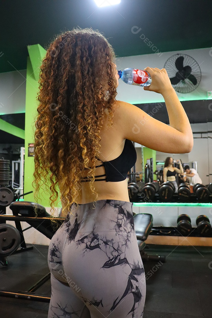 Linda mulher se hidratando depois de executar exercicíos sobre uma academia