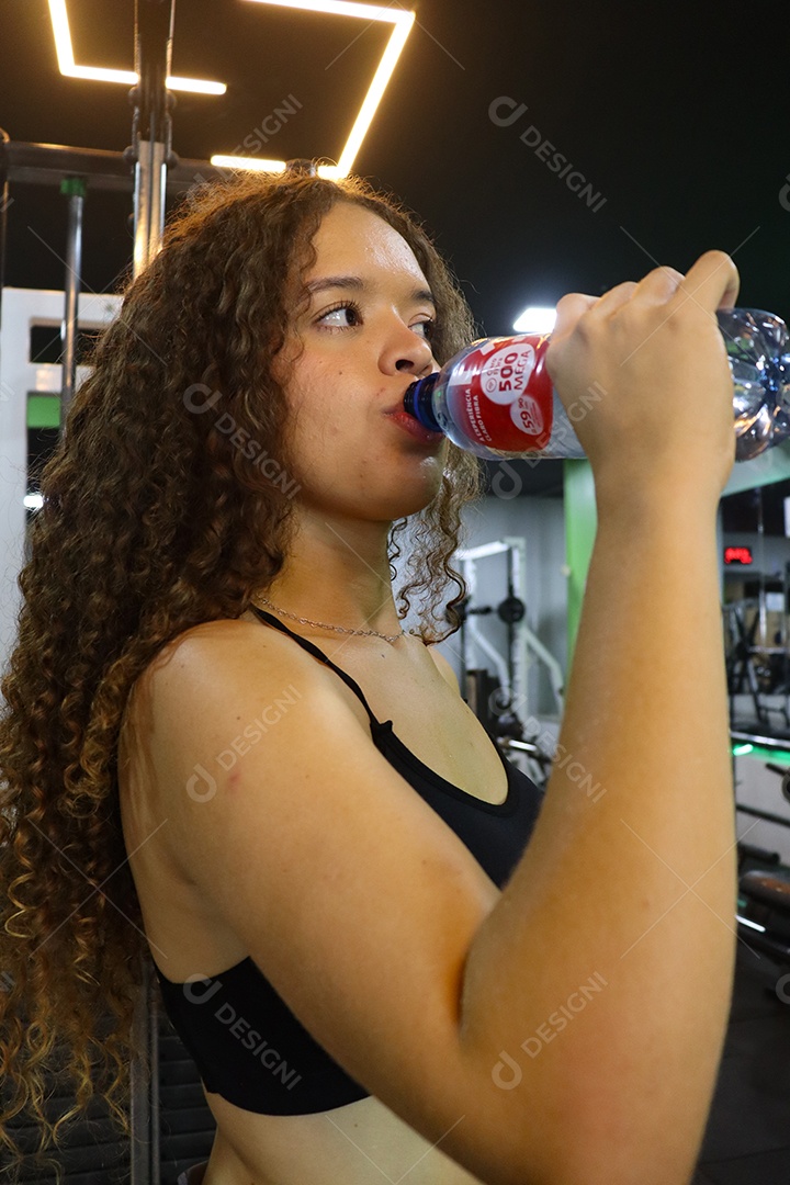 Linda mulher se hidratando depois de executar exercicíos sobre uma academia