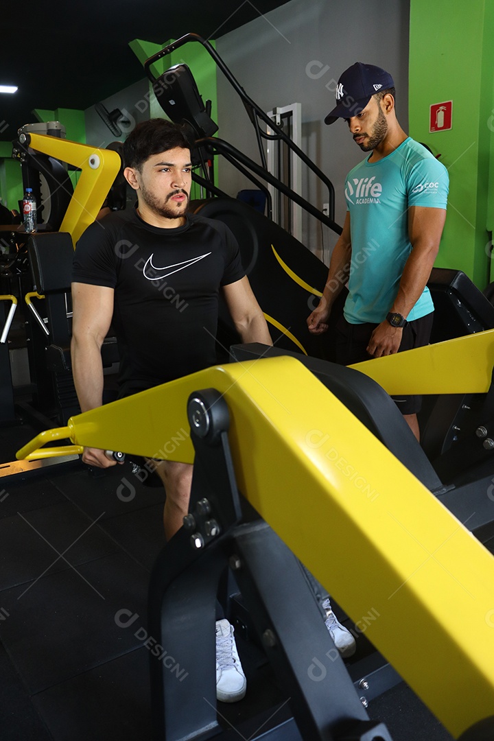 Belo personal trainer ajudando homem executar exercícios sobre uma academia