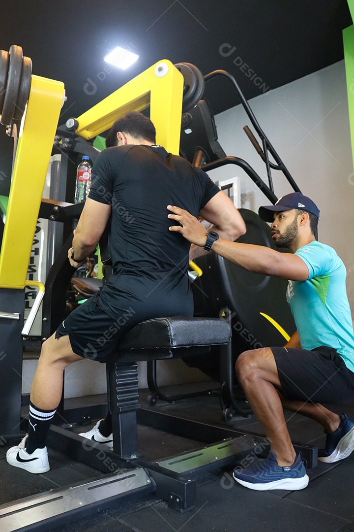 Belo personal trainer ajudando homem executar exercícios sobre uma academia