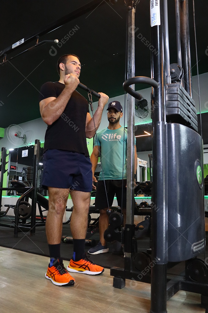 Belo personal trainer ajudando homem executar exercícios sobre uma academia