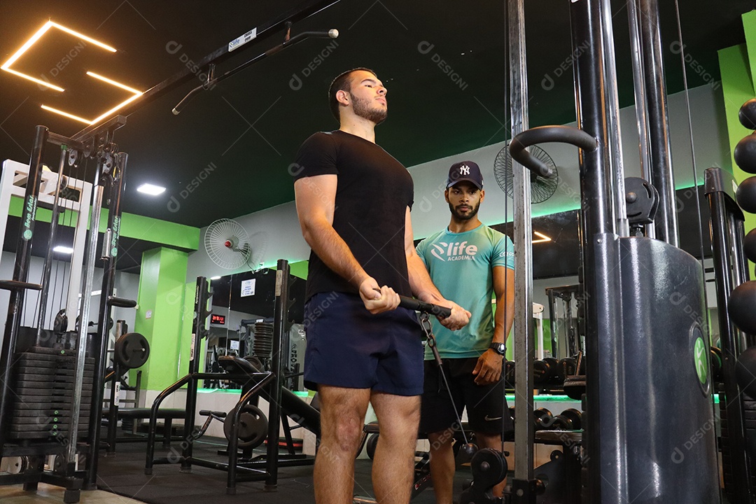 Belo personal trainer ajudando homem executar exercícios sobre uma academia