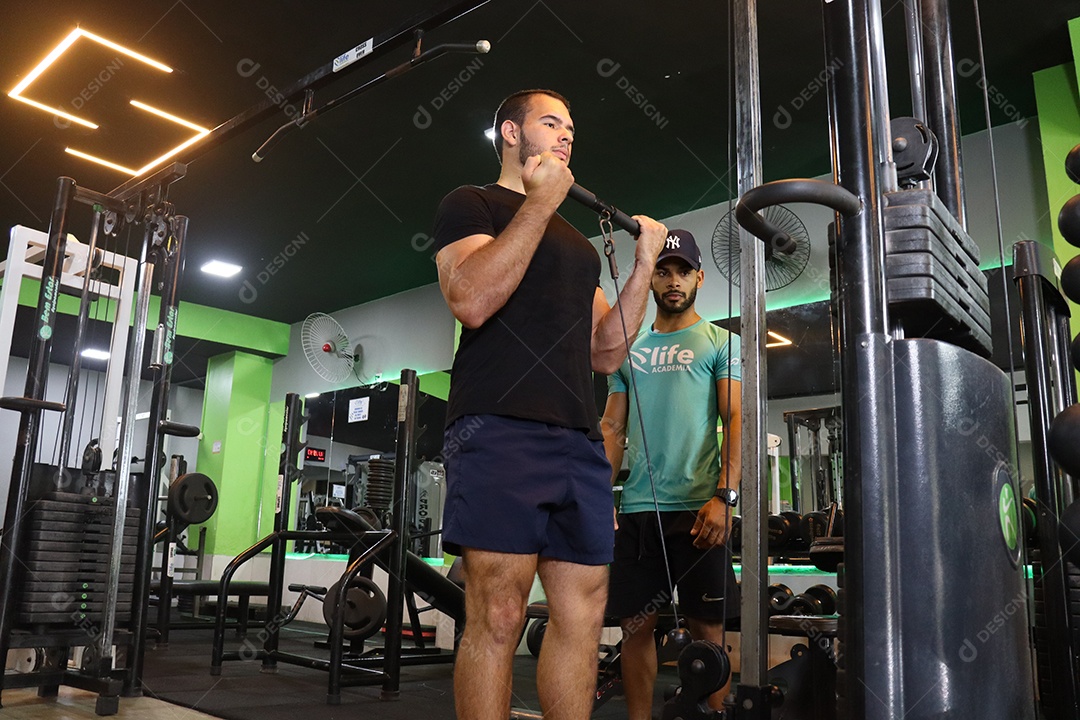 Belo personal trainer ajudando homem executar exercícios sobre uma academia