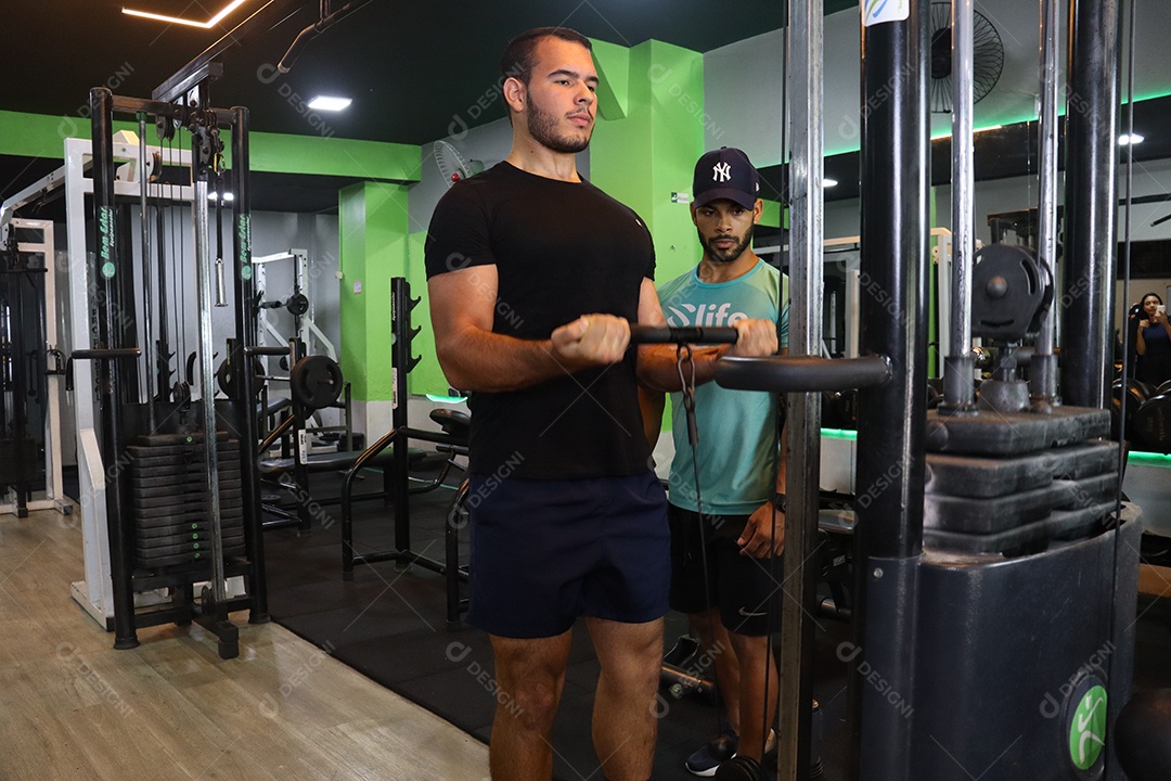 Belo personal trainer ajudando homem executar exercícios sobre uma academia