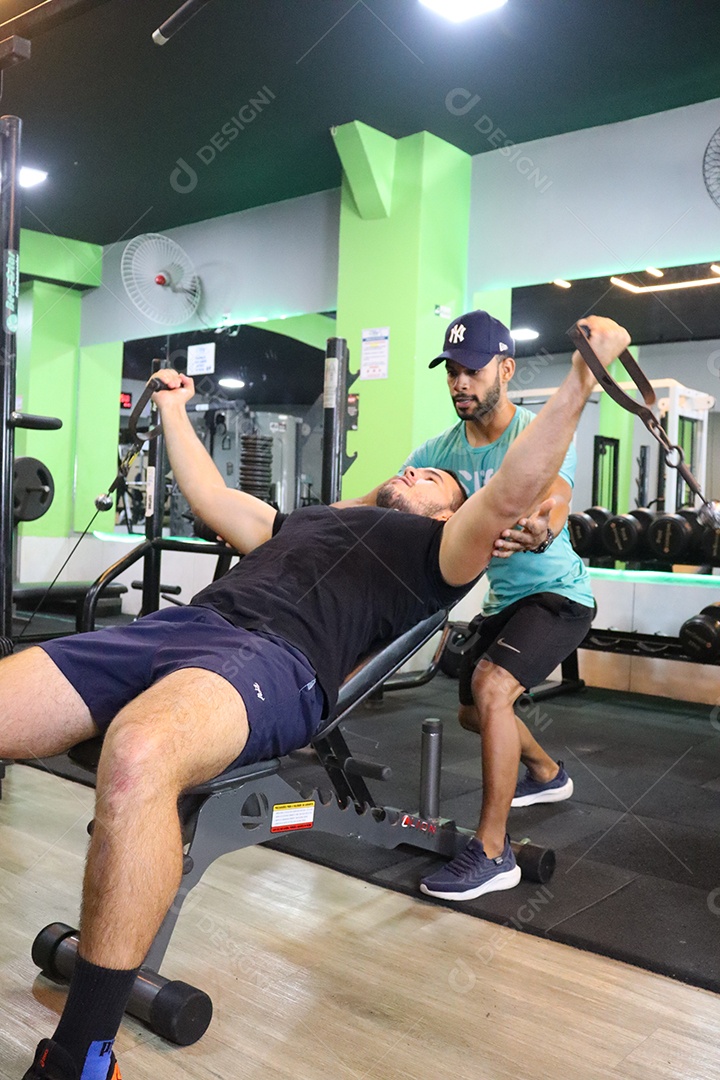 Belo personal trainer ajudando homem executar exercícios sobre uma academia