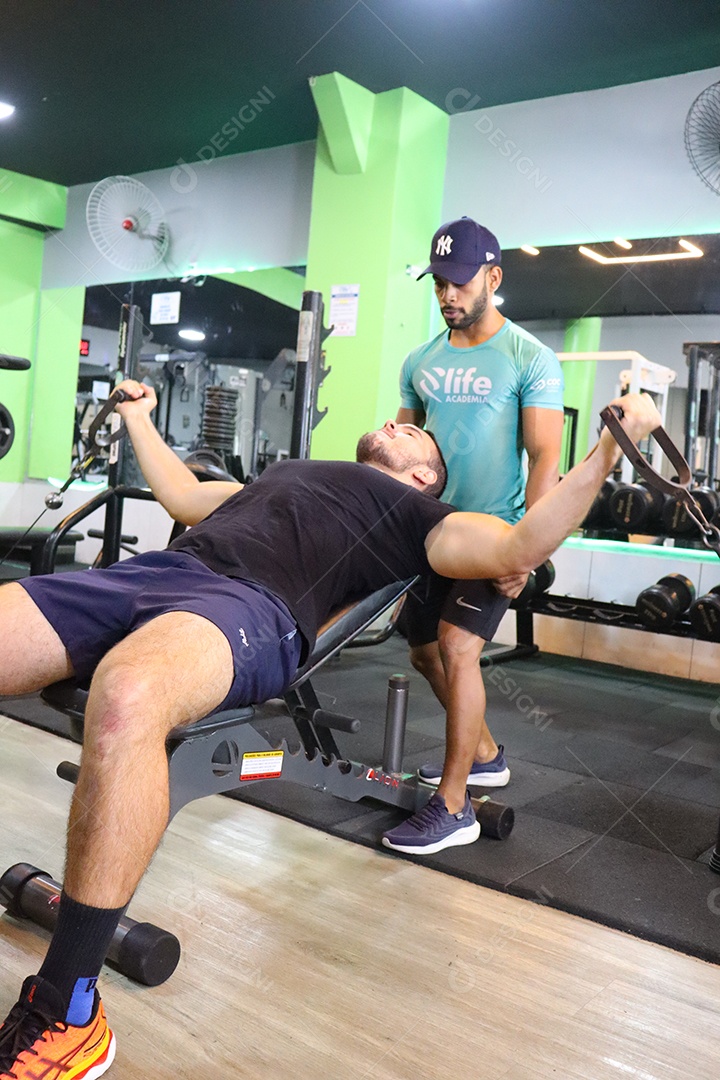 Belo personal trainer ajudando homem executar exercícios sobre uma academia