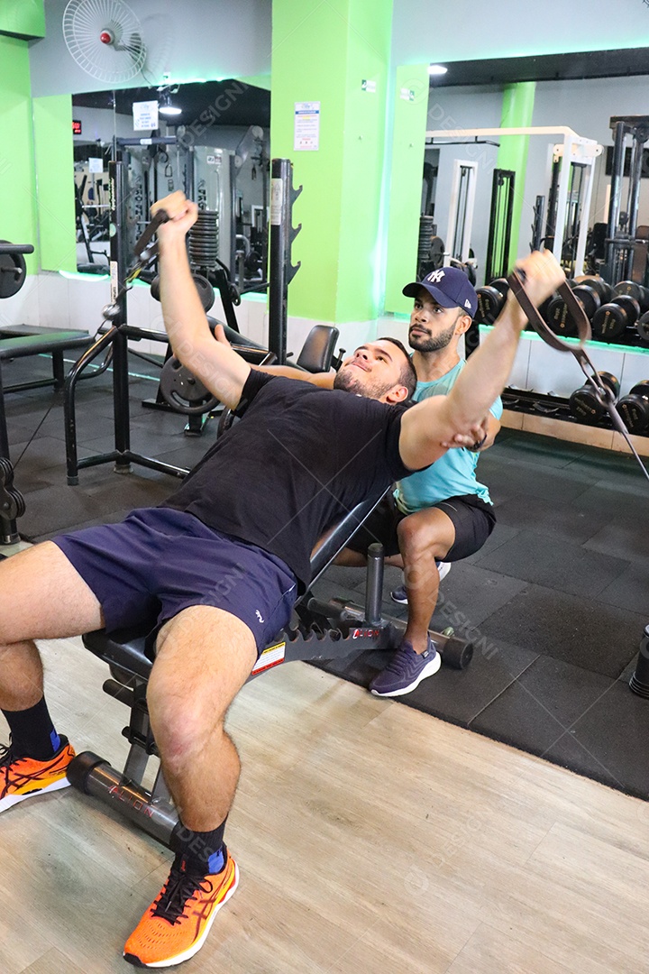 Belo personal trainer ajudando homem executar exercícios sobre uma academia