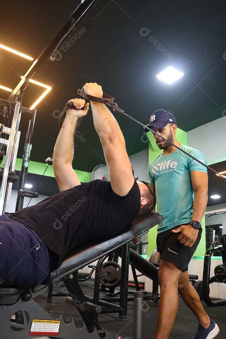 Belo personal trainer ajudando homem executar exercícios sobre uma academia