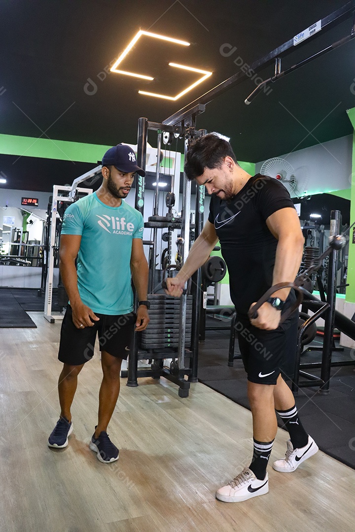 Belo personal trainer ajudando homem executar exercícios sobre uma academia