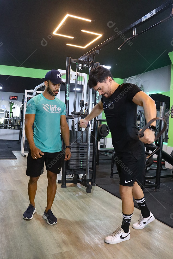 Belo personal trainer ajudando homem executar exercícios sobre uma academia