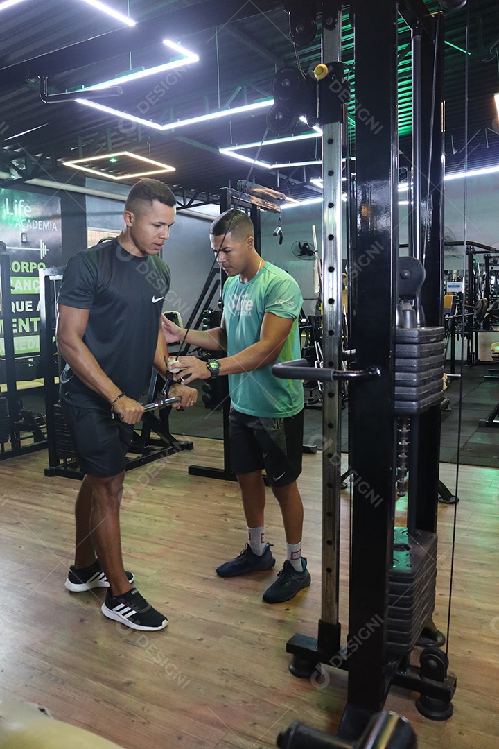 Belo personal trainer ajudando homem executar exercícios sobre uma academia