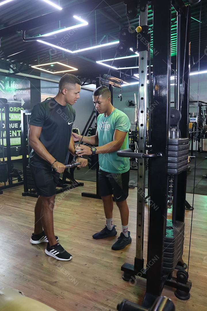 Belo personal trainer ajudando homem executar exercícios sobre uma academia