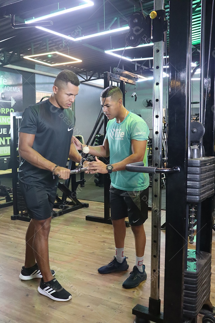 Belo personal trainer ajudando homem executar exercícios sobre uma academia