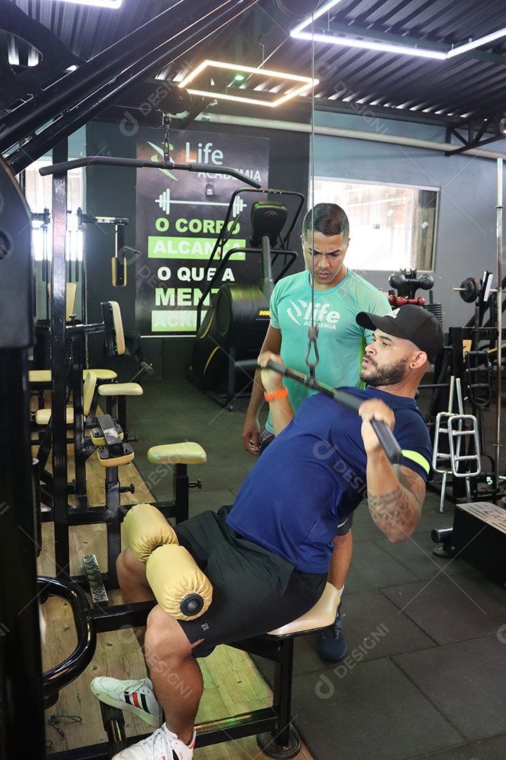 Belo personal trainer ajudando homem executar exercícios sobre uma academia