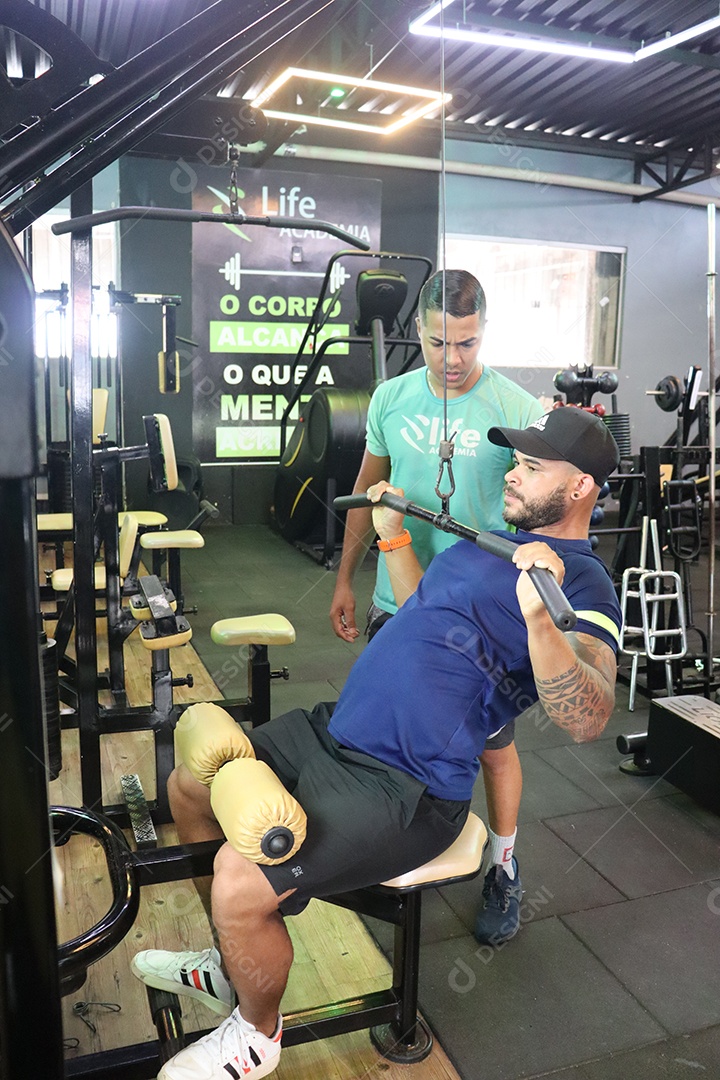 Belo personal trainer ajudando homem executar exercícios sobre uma academia