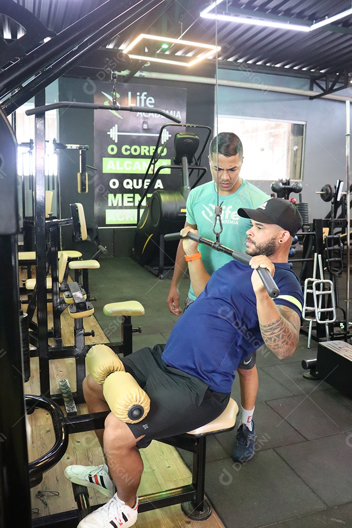 Belo personal trainer ajudando homem executar exercícios sobre uma academia