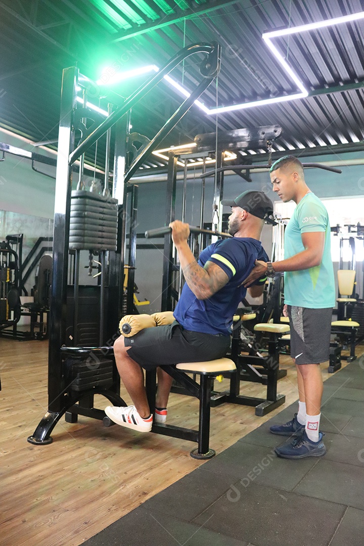 Belo personal trainer ajudando homem executar exercícios sobre uma academia