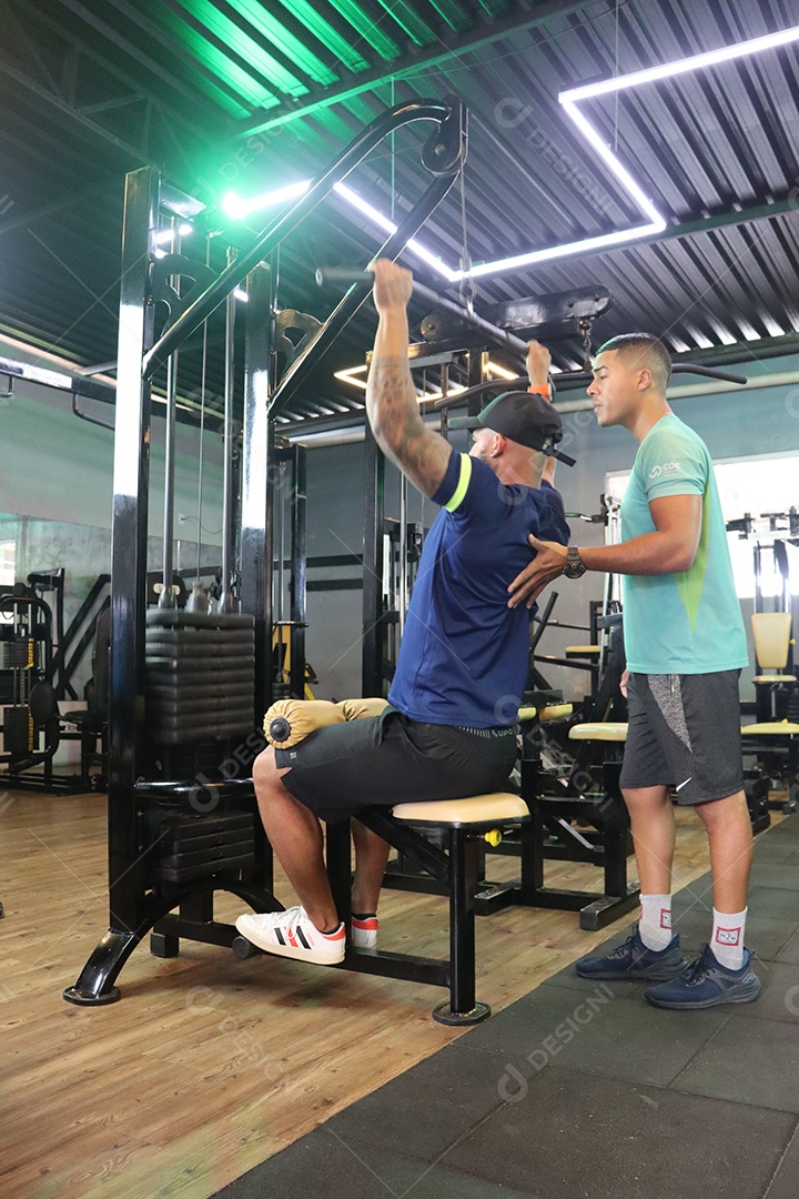 Belo personal trainer ajudando homem executar exercícios sobre uma academia