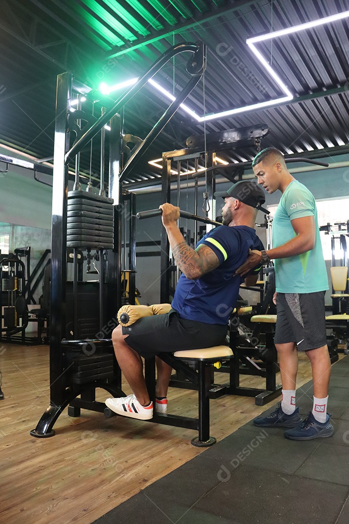 Belo personal trainer ajudando homem executar exercícios sobre uma academia