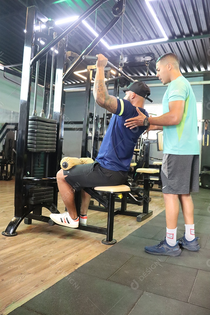 Belo personal trainer ajudando homem executar exercícios sobre uma academia