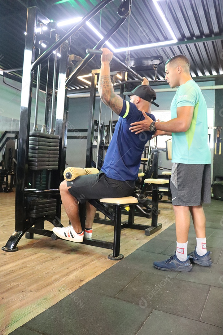 Belo personal trainer ajudando homem executar exercícios sobre uma academia