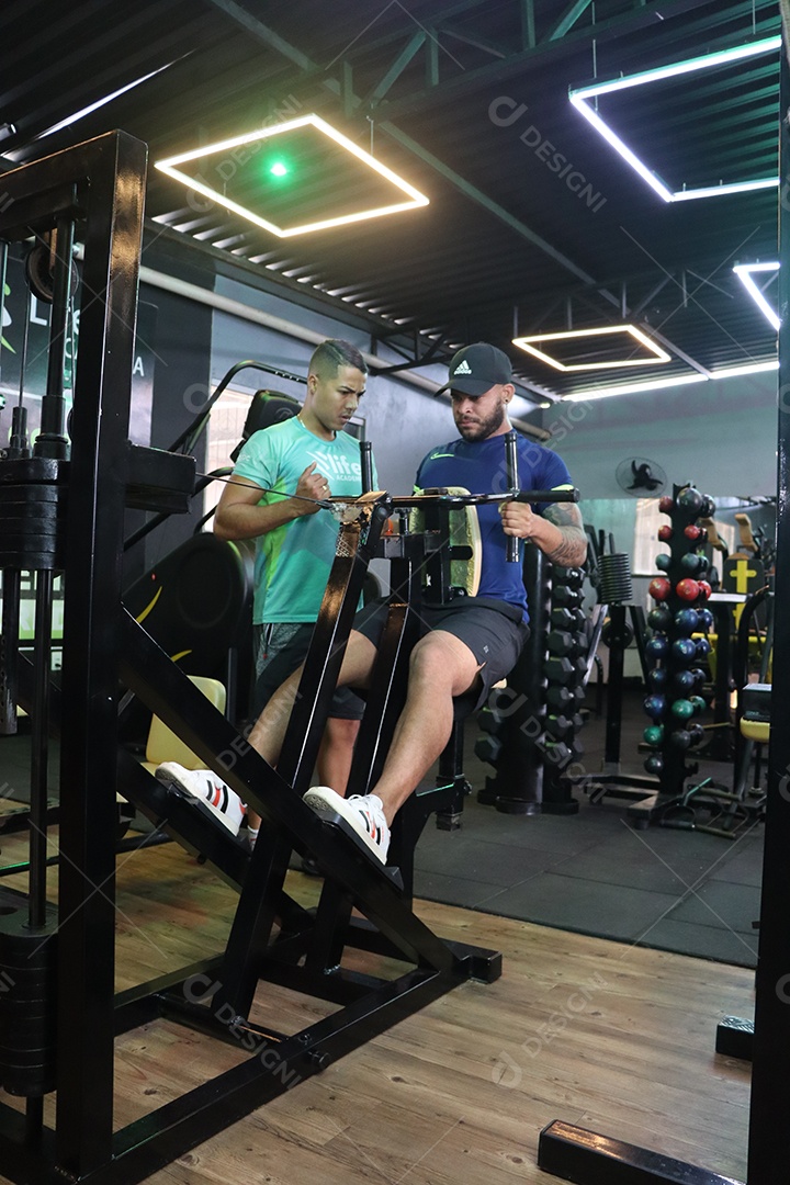 Belo personal trainer ajudando homem executar exercícios sobre uma academia