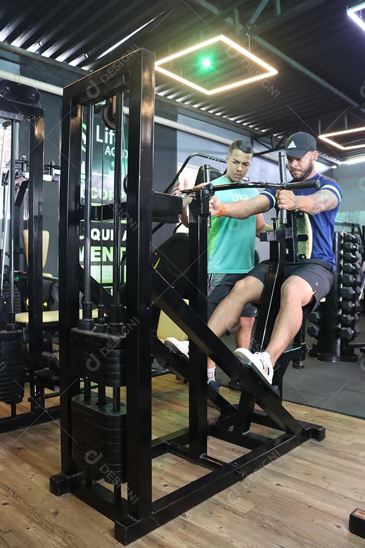 Belo personal trainer ajudando homem executar exercícios sobre uma academia