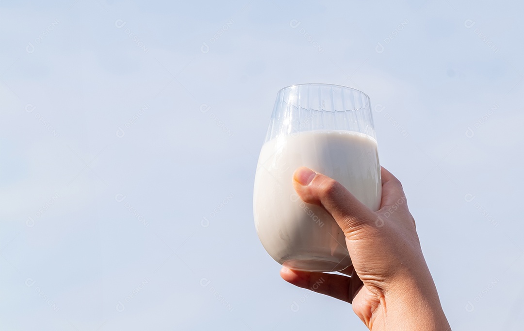 Mão de mãe segurando um copo de leite branco orgânico fresco com fundo de natureza verde e azul