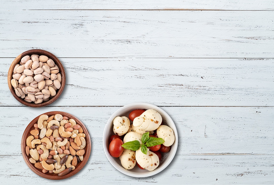 Tigelas Pistaches e Castanhas de caju e amendoins Mozzarella de búfala com tomate cereja e manjericão em uma mesa