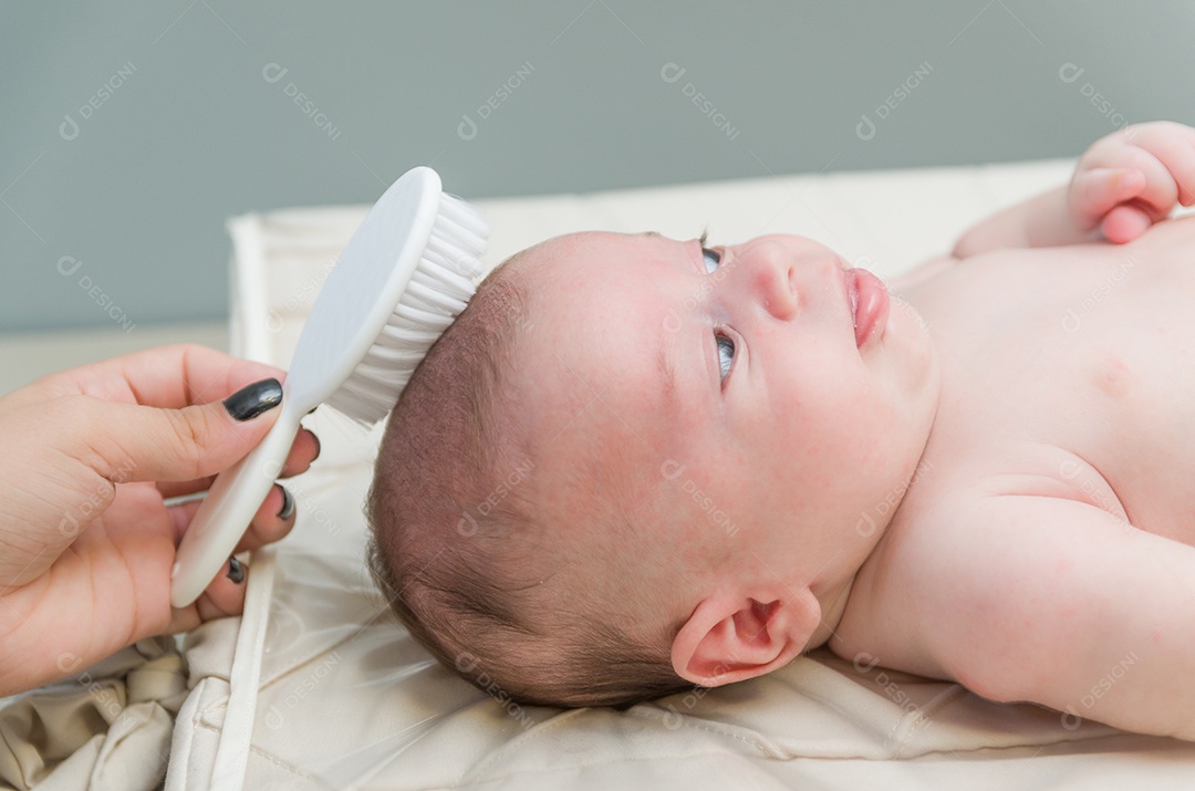 Mãe penteando o cabelo do bebê recém nascido na cama