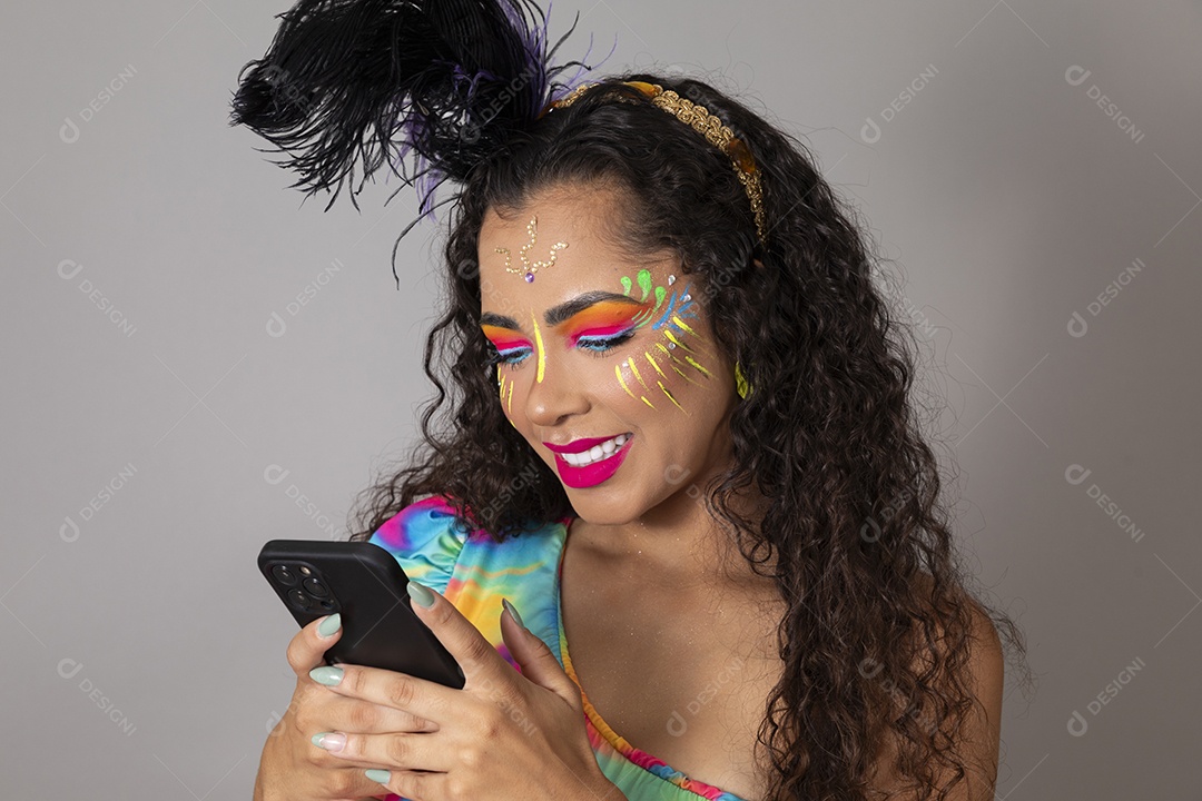 Linda morena do cabelo cacheado sorridente fantasiada segurando smartphone sobre fundo isolado