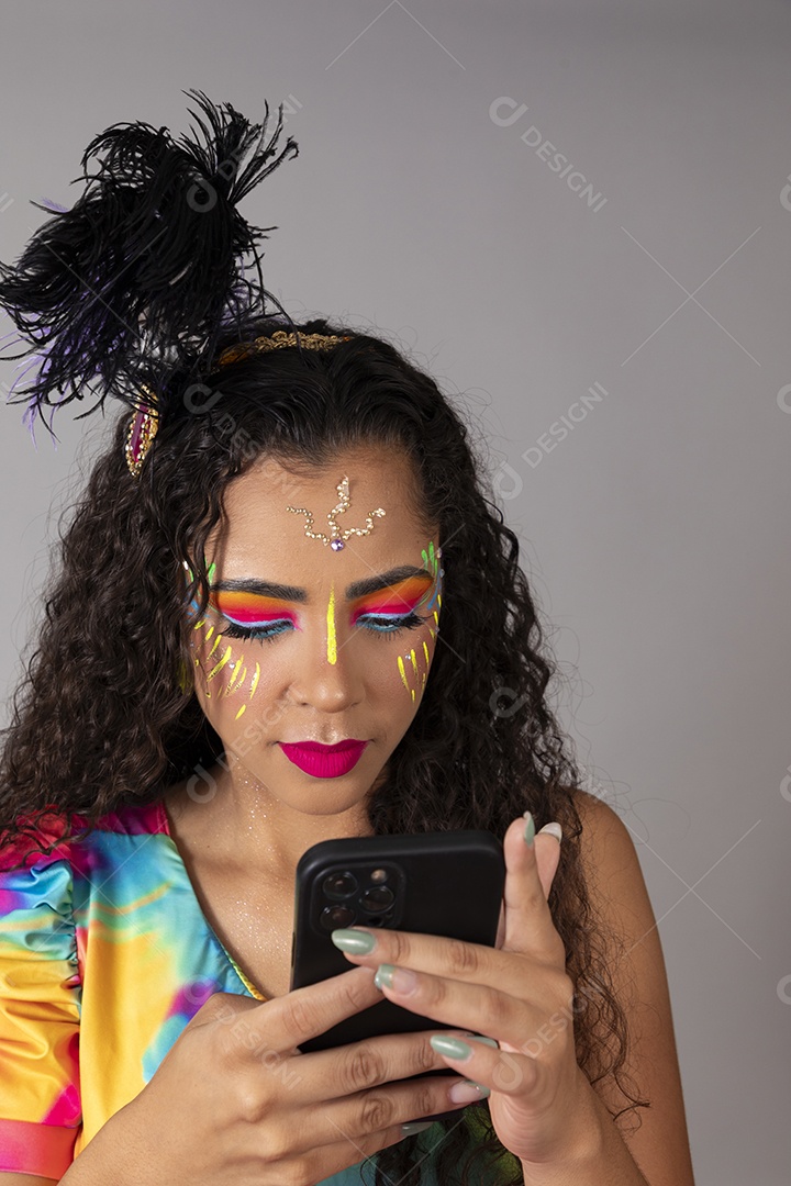 Linda morena do cabelo cacheado sorridente fantasiada segurando smartphone sobre fundo isolado