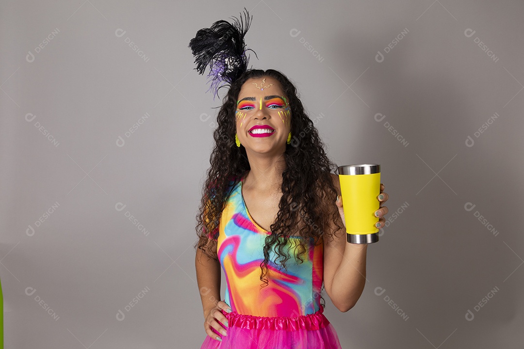 Linda morena do cabelo cacheado sorridente fantasiada segurando copo amarelo sobre fundo isolado
