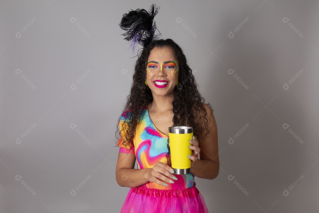 Linda morena do cabelo cacheado sorridente fantasiada segurando copo amarelo sobre fundo isolado