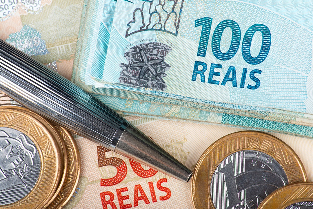 Notas e moedas de real brasileiro com uma caneta