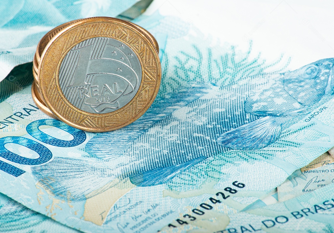 Dinheiro brasileiro com moedas de 1 real espalhadas sobre notas de 100 reais