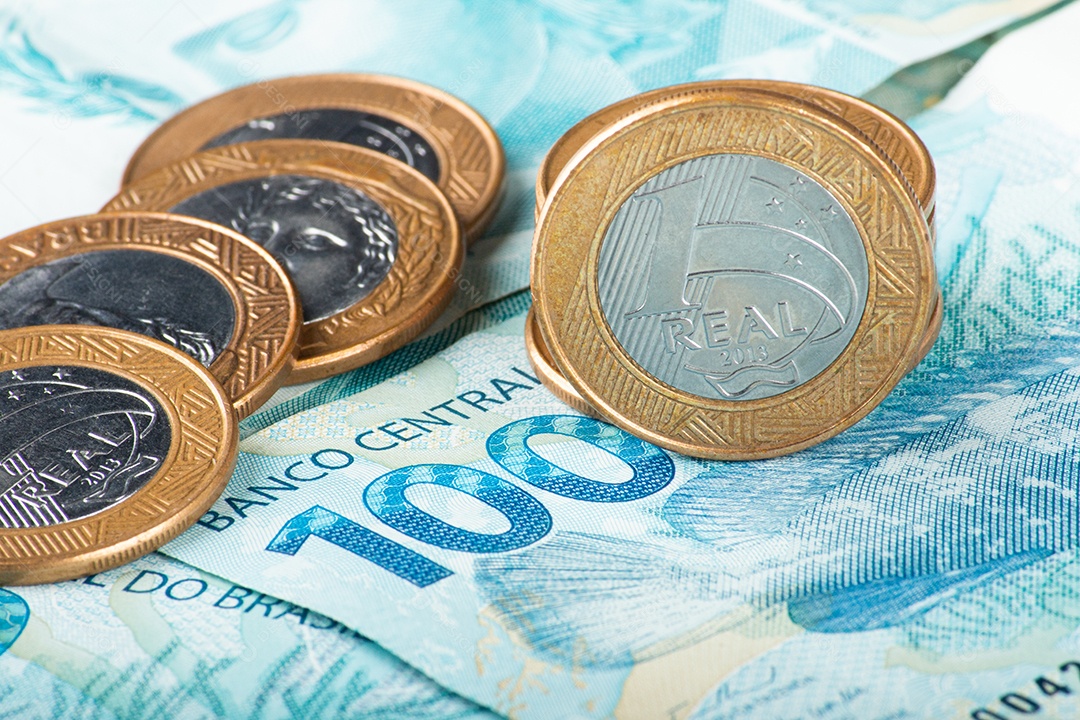 Dinheiro brasileiro com moedas de 1 real espalhadas sobre notas de 100 reais