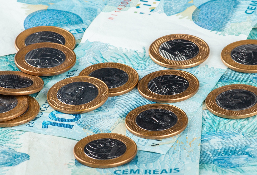 Dinheiro brasileiro com moedas de 1 real espalhadas sobre notas de 100 reais