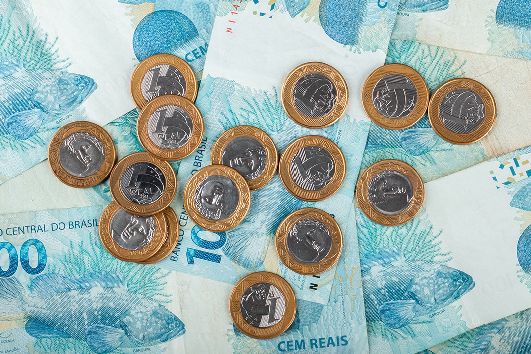 Dinheiro brasileiro com moedas de 1 real espalhadas sobre notas de 100 reais