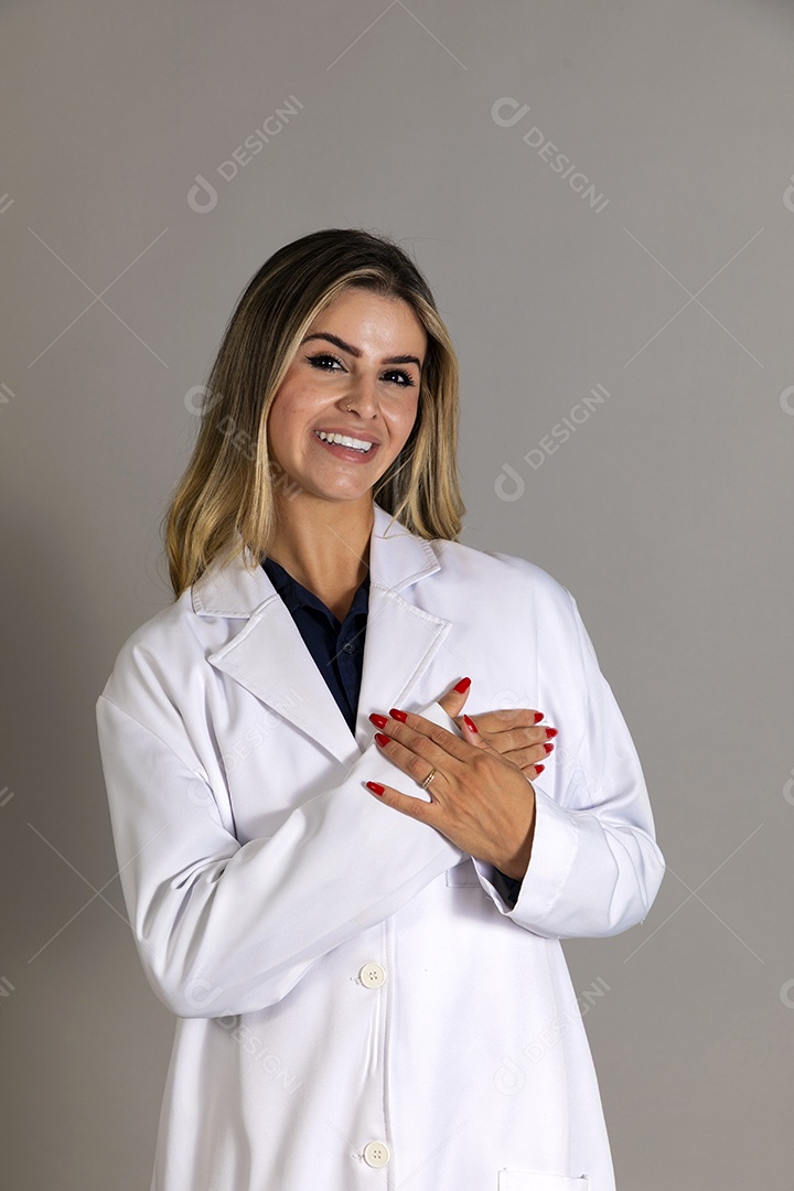 Linda mulher sorridente usando jaleco com a mãos no peito sobre fundo isolado