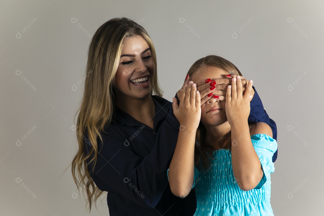 Linda mulher sorridente tampando olho de menina com as mãos sobre fundo isolado