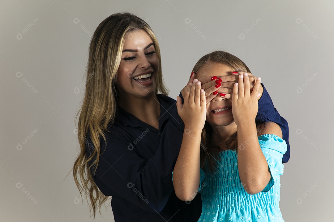 Linda mulher sorridente tampando olho de menina com as mãos sobre fundo isolado