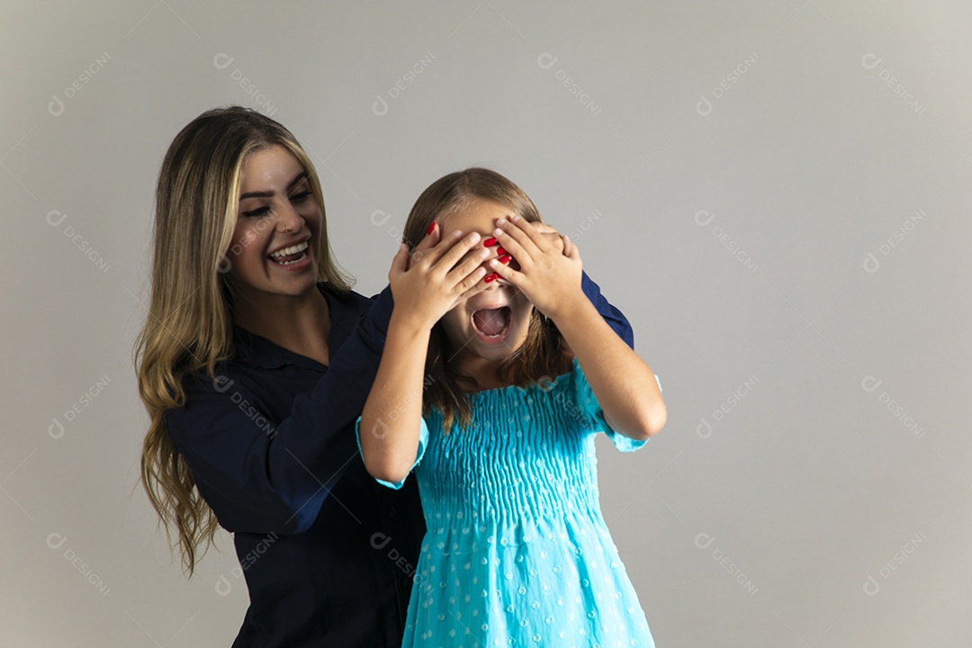 Linda mulher sorridente tampando olho de menina com as mãos sobre fundo isolado