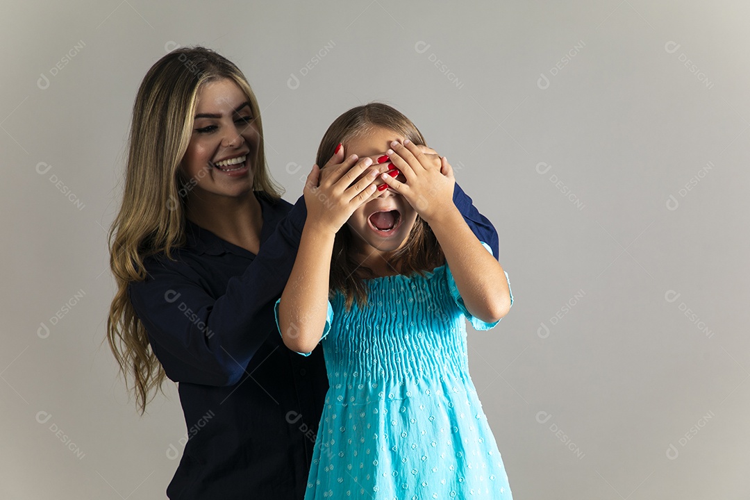 Linda mulher sorridente tampando olho de menina com as mãos sobre fundo isolado