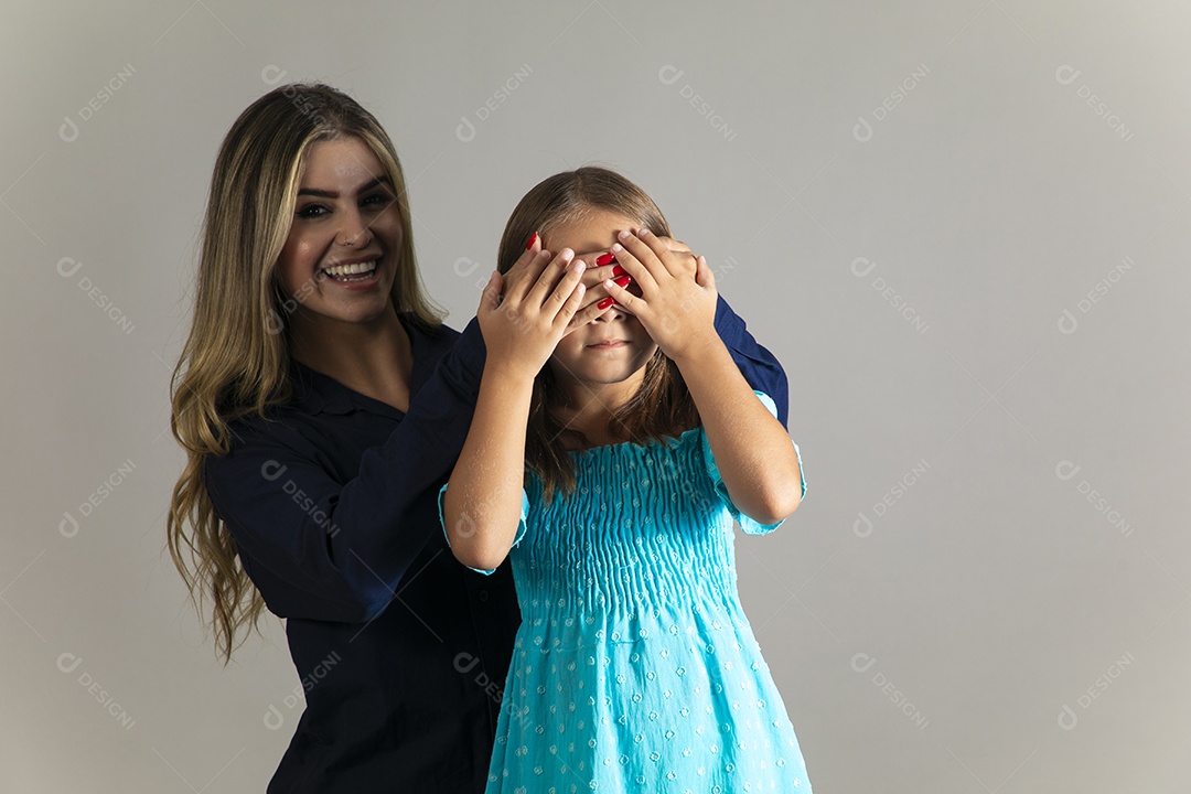 Linda mulher sorridente tampando olho de menina com as mãos sobre fundo isolado