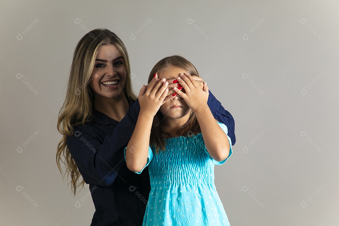 Linda mulher sorridente tampando olho de menina com as mãos sobre fundo isolado