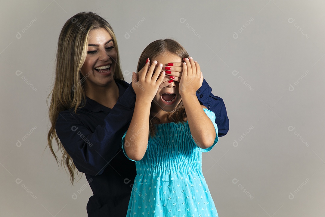 Linda mulher sorridente tampando olho de menina com as mãos sobre fundo isolado
