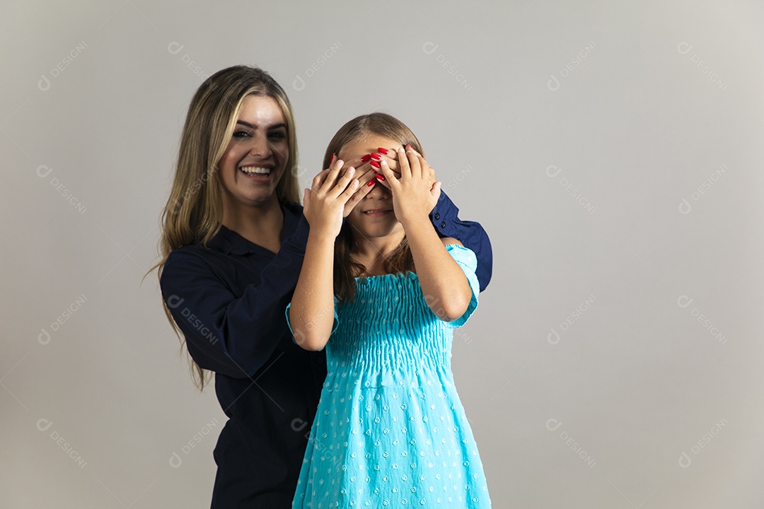 Linda mulher sorridente tampando olho de menina com as mãos sobre fundo isolado